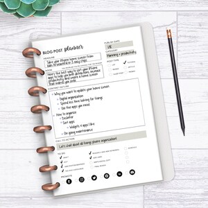 May include: A blog post planner notebook with a white cover and copper-colored binding. The planner includes sections for headlines, outlines, and to-do lists. A pencil rests on the right side. The text on the planner reads "BLOG POST planner".