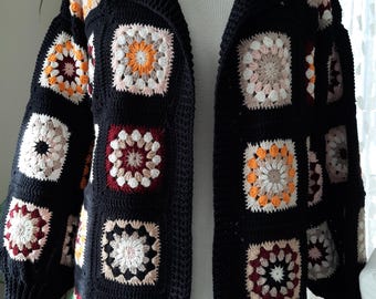 May include: A long black crochet cardigan with colorful granny square patterns. The cardigan has a collar and long sleeves.