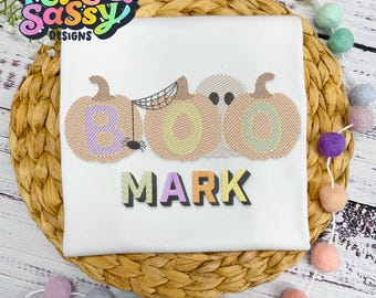 May include: White t-shirt with a Halloween-themed design featuring three pumpkins with the letters "BOO" and a ghost. The name "MARK" is embroidered below the pumpkins.