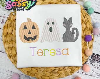 May include: White t-shirt with a pumpkin, ghost, and black cat design. The name "Teresa" is embroidered in rainbow colors below the design.