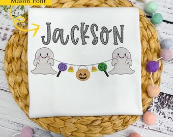 May include: White t-shirt with a Halloween-themed design featuring a ghost, candy, and a pumpkin. The name "Jackson" is embroidered in a black font.