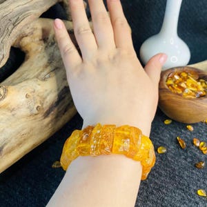 May include: A bracelet made of irregular, polished amber pieces. The amber is a warm, translucent yellow-orange colour. The bracelet is worn on a wrist.