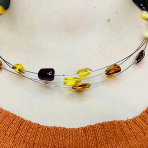 May include: A multi-strand necklace with amber beads in shades of yellow, brown, and orange. The necklace is made of thin silver wires.