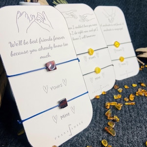 May include: Friendship bracelets with amber-coloured beads and square beads on blue and black cords. The cards say "Yours" and "Mine" with heart symbols. The text on the cards reads "We'll be best friends forever because you already know too much."