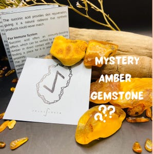 May include: Several pieces of raw amber gemstones in shades of yellow and gold. The image features a card with a rune symbol and the words "MYSTERY AMBER GEMSTONE" and "PRANA AMBER". The amber pieces vary in size and shape.