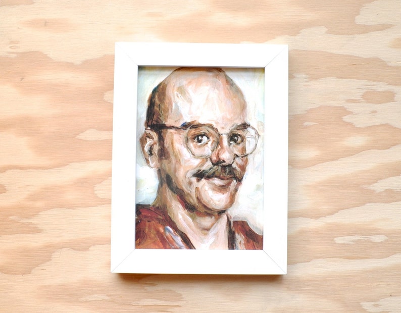 May include: A framed painting of a man with a mustache and glasses. The man is wearing a brown shirt and has a light complexion. The painting is done in a realistic style.
