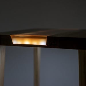 May include: A dark wood table with a clear resin inlay that has a warm, golden glow. The table has four legs made of light wood.