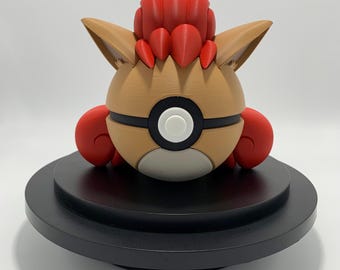 May include: A 3D-printed figure of a Pokémon character, featuring a tan body, red accents, and a black and white circular design. The figure is on a black circular base, showcasing a detailed and colorful design.