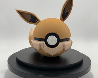 May include: A brown and tan Eevee Pokemon figure in a Pokeball form. The figure is on a black circular base.