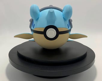 May include: A 3D-printed figure of a cartoon character, featuring a light blue head with two large ears and a dark gray crest. The body is tan and round, with a black and white circular design. The figure is on a black circular base.