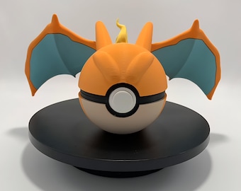 May include: A 3D-printed orange and tan Poke Ball with Charizard wings and features. The wings are teal and orange. The ball has a white button and is on a black circular stand.