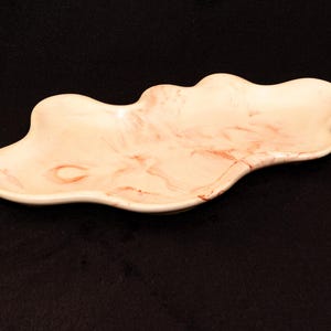 Puede incluir: Un plato decorativo en forma de nube con una base color crema y veteado marrón rojizo. El plato tiene un acabado liso y brillante y una profundidad poco profunda. La forma única y las variaciones de color lo convierten en una pieza elegante.