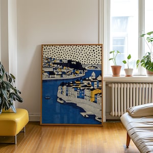 K&ouml;nnte beinhalten: Gerahmter Kunstdruck mit einer Stadtlandschaft und einem Fluss. Das Kunstwerk zeigt Geb&auml;ude in Blau, Gelb und Wei&szlig;, mit einem gepunkteten Muster im oberen Bereich. Der Rahmen hat eine warme braune Farbe. Das Bild h&auml;ngt in einem Raum.