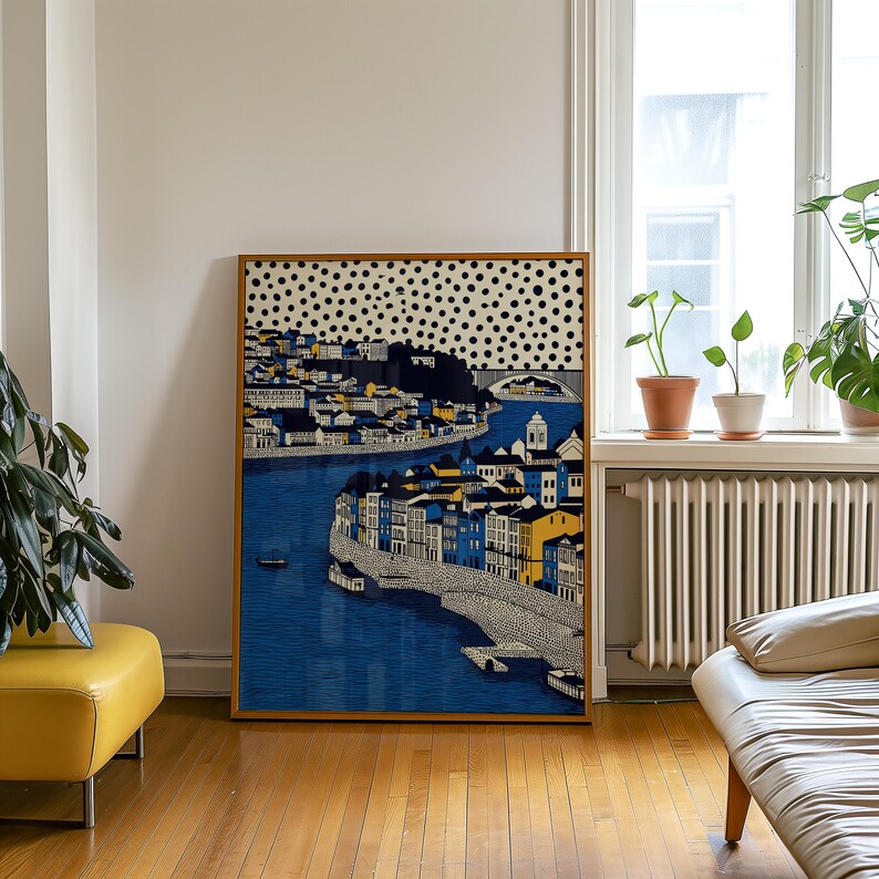 K&ouml;nnte beinhalten: Gerahmter Kunstdruck mit einer Stadtlandschaft und einem Fluss. Das Kunstwerk zeigt Geb&auml;ude in Blau, Gelb und Wei&szlig;, mit einem gepunkteten Muster im oberen Bereich. Der Rahmen hat eine warme braune Farbe. Das Bild h&auml;ngt in einem Raum.