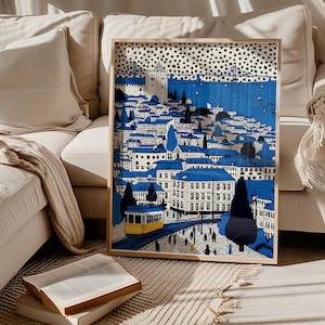 May include: A framed art print depicting a cityscape with blue rooftops and buildings. A yellow trolley car travels on tracks. The artwork has a blue and white color scheme with a dotted pattern at the top. The print is displayed on a beige sofa.