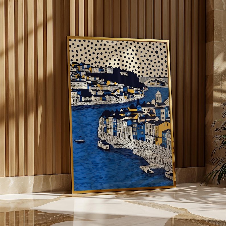 K&ouml;nnte beinhalten: Gerahmter Kunstdruck mit einer detaillierten Illustration einer K&uuml;stenstadt mit blauem Wasser und Geb&auml;uden in Wei&szlig;, Gelb und Blau. Das Kunstwerk hat einen goldenen Rahmen und einen gepunkteten Hintergrund. Der Druck wird vor einer Holzwand ausgestellt.