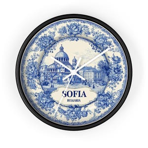 May include: Circular wall clock with a black surround, featuring a blue and white floral pattern. The clock face displays a detailed illustration of a building, with the text "SOFIA BULGARIA". White clock hands show the time.