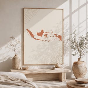 Peut inclure: Une impression murale rectangulaire présentant une carte de l'Indonésie de couleur terre cuite centrée sur un fond crème. Le design comprend des motifs de lignes fines et courbes dans les coins, encadré par une bordure en bois clair.