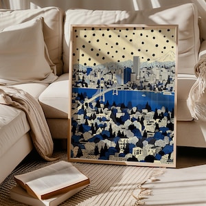 May include: Framed art print depicting a city skyline with a bridge over a blue body of water. The artwork features a blue and white color palette with a dotted background and a mountain in the distance. The print is displayed on a beige sofa.