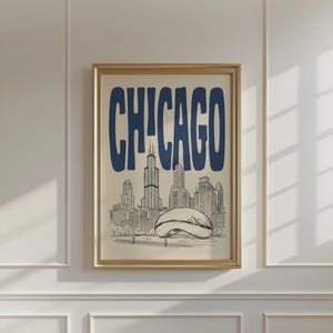 Può includere: Una stampa artistica incorniciata con la parola CHICAGO in grandi lettere blu scuro. Sotto il testo si trova un dettagliato disegno a linee in bianco e nero dello skyline di Chicago, che include l'iconica scultura a forma di fagiolo in primo piano.