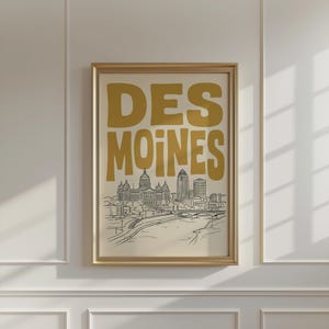 Peut inclure: Une affiche encadrée présentant le texte DES MOINES en grandes lettres grasses jaune moutarde au-dessus d'un dessin au trait noir et blanc de la ligne d'horizon de Des Moines, incluant le capitole de l'Iowa et un pont sur la rivière.