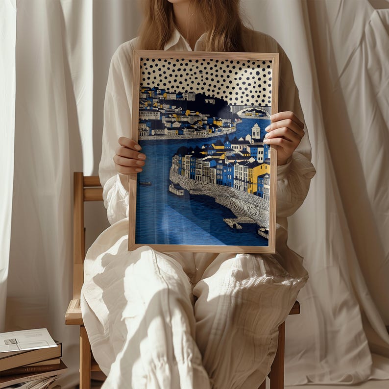 K&ouml;nnte beinhalten: Ein gerahmter Kunstdruck, der eine Stadtlandschaft mit blauem Wasser und Geb&auml;uden in Blau-, Gelb- und Wei&szlig;t&ouml;nen zeigt. Das Kunstwerk hat oben ein gepunktetes Muster und ist in einem hellen Holzrahmen gehalten.
