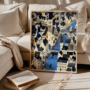 May include: A framed art print showing a stylized cityscape with buildings, a river, and bridges. The artwork uses blue, black, yellow, and cream colours. The print is displayed on a beige rug, with a book and a sofa in the background.