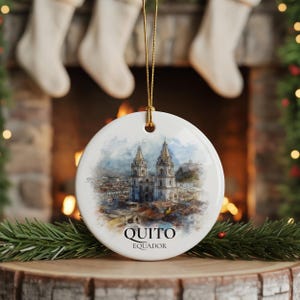 May include: Round white ceramic Christmas ornament with a watercolour painting of a cathedral in Quito, Ecuador. The ornament has a gold string for hanging and the city name is printed below the image.