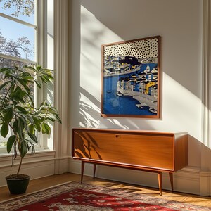 K&ouml;nnte beinhalten: Ein gerahmtes Kunstwerk, das eine K&uuml;stenstadt mit blauem Wasser und farbenfrohen Geb&auml;uden zeigt. Das Kunstwerk h&auml;ngt &uuml;ber einem modernen Holzschrank aus der Mitte des Jahrhunderts mit konischen Beinen. Eine Topfpflanze steht in der N&auml;he eines gro&szlig;en Fensters.