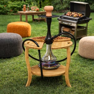 May include: A black hookah with a glass base and a clay bowl sits on a bamboo table. The table has two levels and curved legs. The hookah is surrounded by a green lawn and several poufs.
