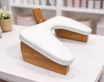 May include: A white, U-shaped manicure arm rest with a wooden base and a small wooden phone holder. The arm rest is on a white table. The background includes shelves with various products.