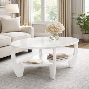 May include: A white oval coffee table with a lower shelf. The table has curved legs and a glossy finish. A vase of flowers and books are on the table. The table is in a living room setting.