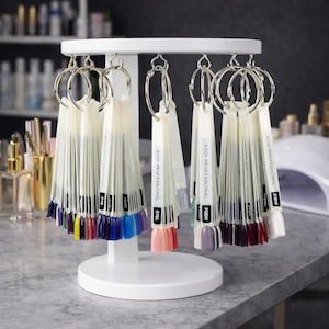 May include: A white nail polish display stand with multiple color swatch fans. Each fan is attached to a silver ring and displays a variety of nail polish colors, including pinks, blues, and purples. The text "KODI PROFESSIONAL" is visible on each fan.