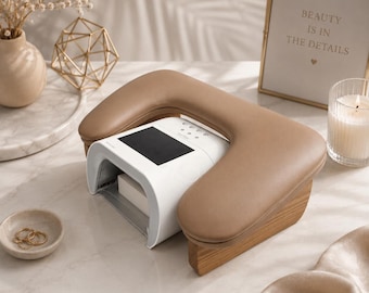 May include: A white nail lamp with a black display is set on a light-colored wooden base, with a tan armrest. A small gold-framed sign reads "BEAUTY IS IN THE DETAILS." A lit candle and small dish with rings are also present.