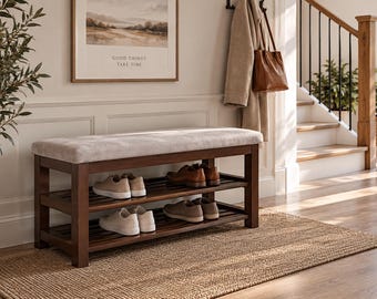 May include: A rectangular wooden shoe bench with a light gray upholstered seat cushion and two slatted shelves for storage. The frame is finished in a dark brown wood tone, and the bench is positioned on a woven rug in a home entryway setting.