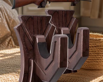 May include: Two dark brown wooden gun racks with a decorative design. The racks are mounted on a wall and have two hooks each. The hooks are designed to hold rifles or shotguns.