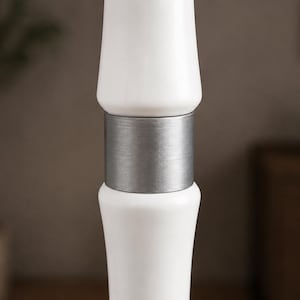 May include: A vertical lamp post section featuring two smooth, glossy white cylindrical components separated by a central brushed silver metal band. The design consists of a symmetrical arrangement with the metallic accent positioned between the white parts.