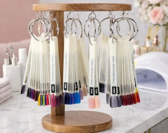 May include: A wooden nail polish color display stand with multiple color swatches. Each swatch is labeled with a code and attached to a metal ring. The stand is made of light brown wood and sits on a white surface. The nail polish colors include shades of pink, blue, purple, and red.