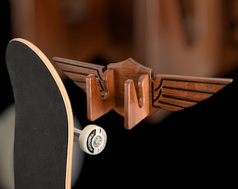 May include: A wooden skateboard wall mount with a wing design. The mount is made of dark wood with black accents. A skateboard is hanging on the mount.