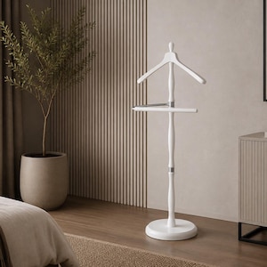 May include: A white wooden valet stand featuring a contoured coat hanger at the top, a horizontal bar for trousers, and a central vertical post supported by a circular base. The design includes silver-toned metal accents connecting the components.