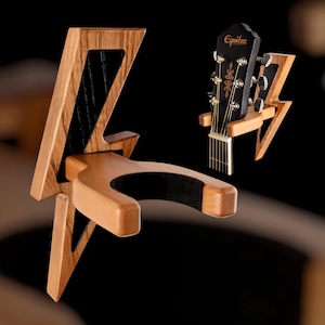 Pode incluir: Um suporte de parede para guitarra de madeira em forma de raio. O suporte tem um forro de feltro preto para proteger o acabamento da guitarra. O suporte é projetado para segurar uma guitarra acústica ou elétrica.