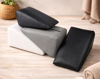 May include: A collection of black, white, and gray wedge-shaped pillows. The pillows are made of a smooth material and are arranged in a layered composition. The pillows are on a light wood surface.