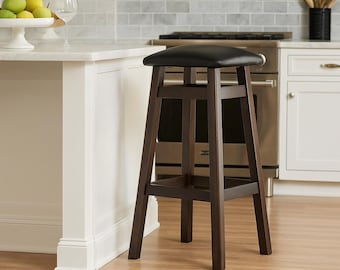 May include: A dark brown wooden bar stool with a black leather seat. The stool has a square seat and four angled legs. The kitchen stool is placed in front of a white countertop and a stainless steel oven.