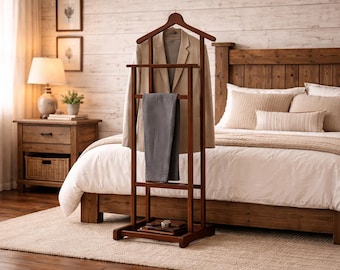 May include: A dark brown wooden valet stand featuring a top hanger for a blazer, a horizontal bar for trousers, and a lower shelf. The stand holds a beige blazer and a pair of grey trousers, with a small object resting on the bottom base shelf.