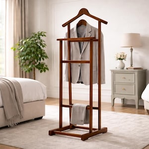 May include: A wooden valet stand with a jacket and trousers hanging on it. The stand is a dark brown color and has a hanger for the jacket and a bar for the trousers. The jacket is light gray. The stand is in a bedroom.