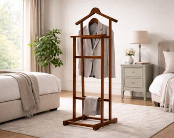May include: A wooden valet stand with a jacket and trousers hanging on it. The stand is a dark brown color and has a hanger for the jacket and a bar for the trousers. The jacket is light gray. The stand is in a bedroom.