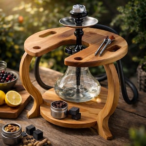 May include: A wooden hookah set with a clear glass water chamber and a black stem. The hookah sits on a wooden stand with a curved design. Accessories include a metal bowl, charcoal, and tongs. The background is blurred with greenery.