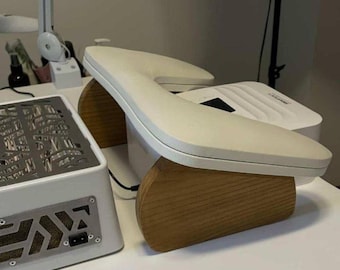 May include: A white nail lamp with a curved design, resting on a wooden base. A white rectangular device with a metal grate is to the left. The items are on a white surface.