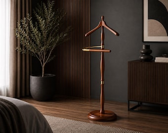 May include: A freestanding wooden valet stand featuring a dark brown finish, a contoured coat hanger top, and a horizontal bar for trousers. The central post is accented with gold-toned metal hardware, and the unit rests on a circular base.