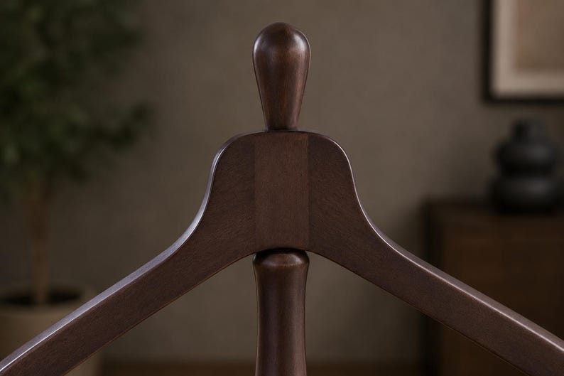 May include: A dark brown wooden clothes hanger featuring a smooth, curved frame and a central vertical post topped with a rounded, finial-like knob. The wood grain is visible across the surface, showcasing a polished, uniform finish throughout.